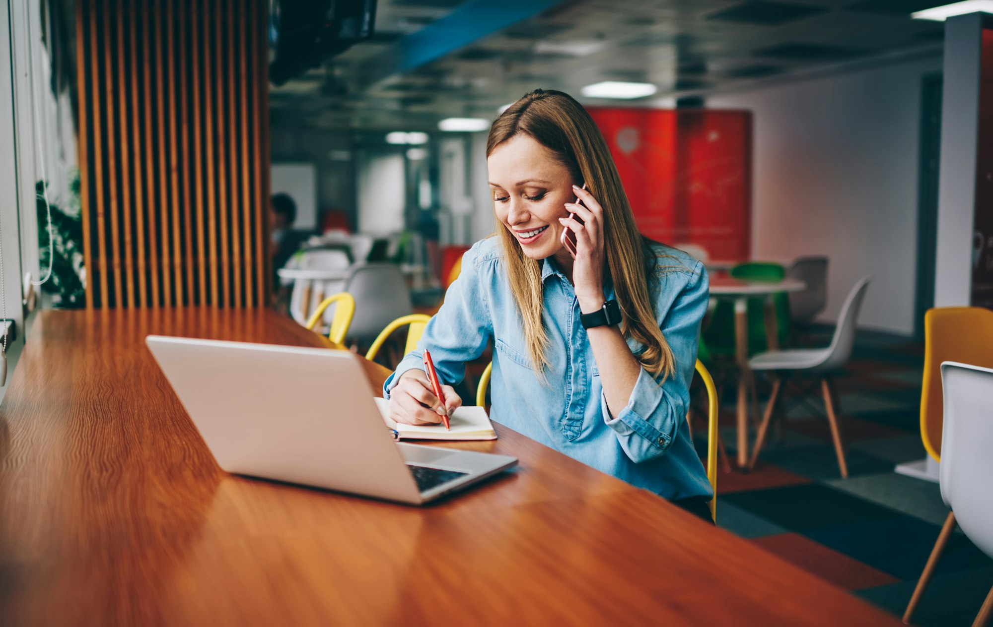 Smiling woman talking on phone and taking notes